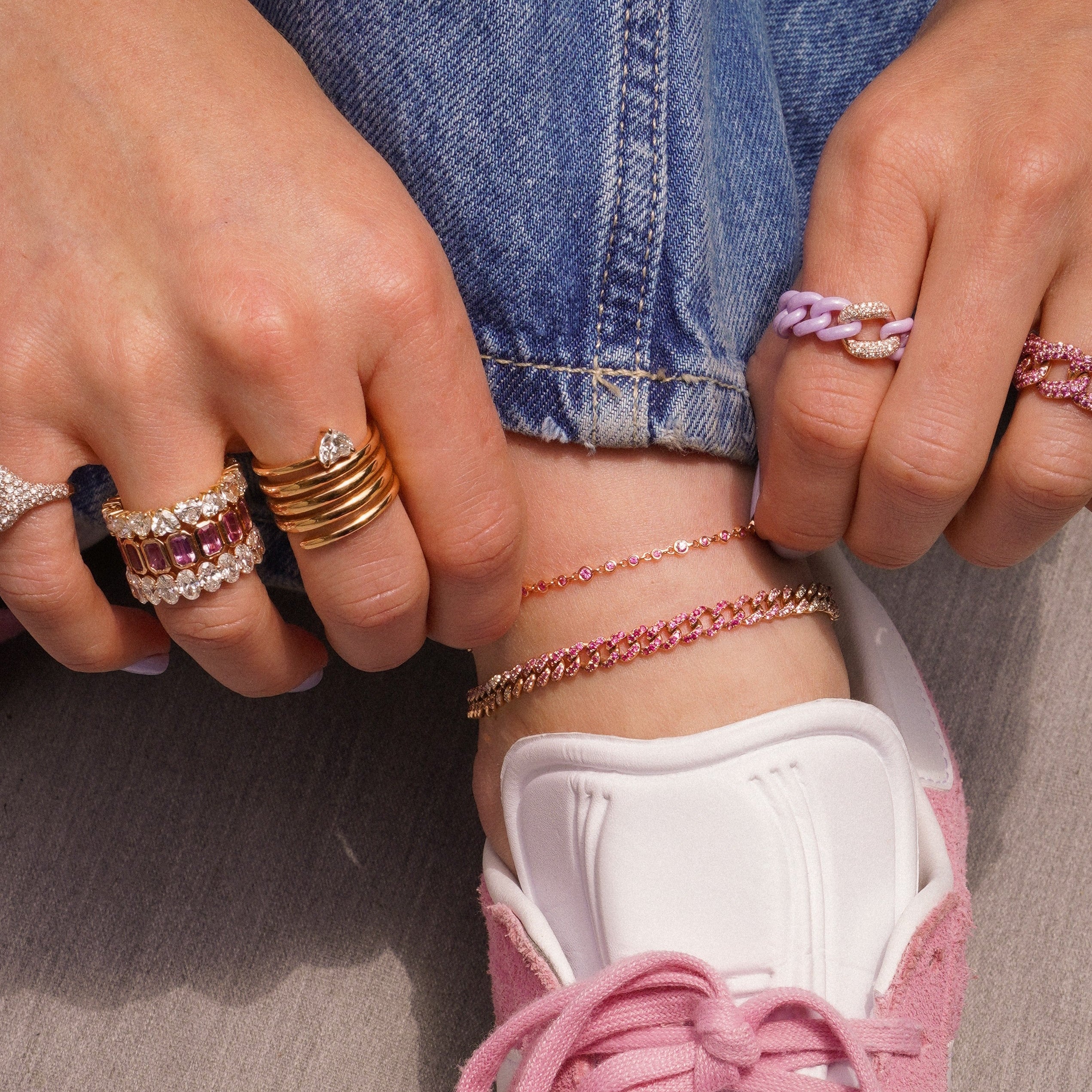 Model wearing stacked pink sapphire anklets on ankle with jeans rolled up, styled with pink sneakers and multiple diamond and gold rings