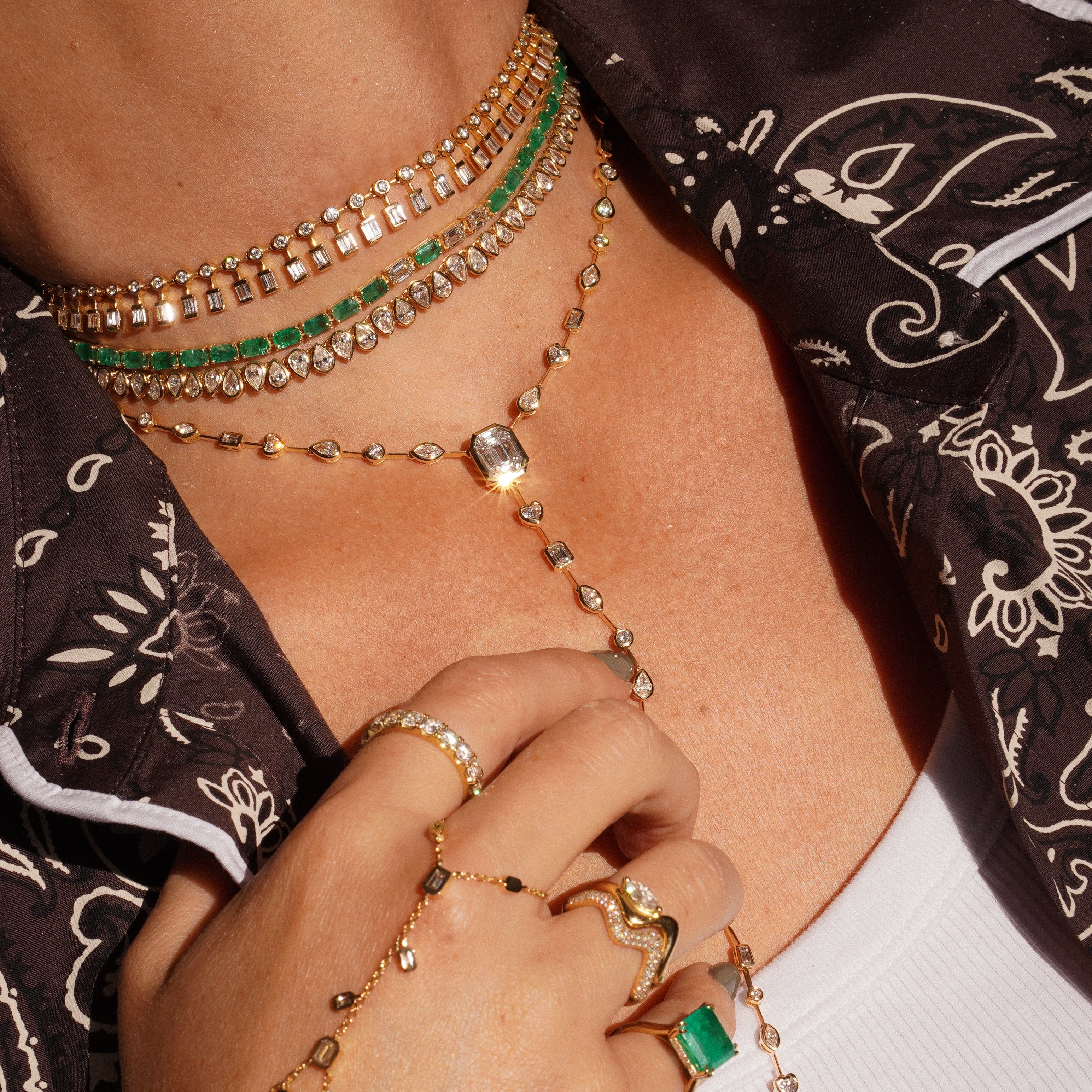 Close-up of a person wearing multiple gold and green gemstone necklaces and bracelets.