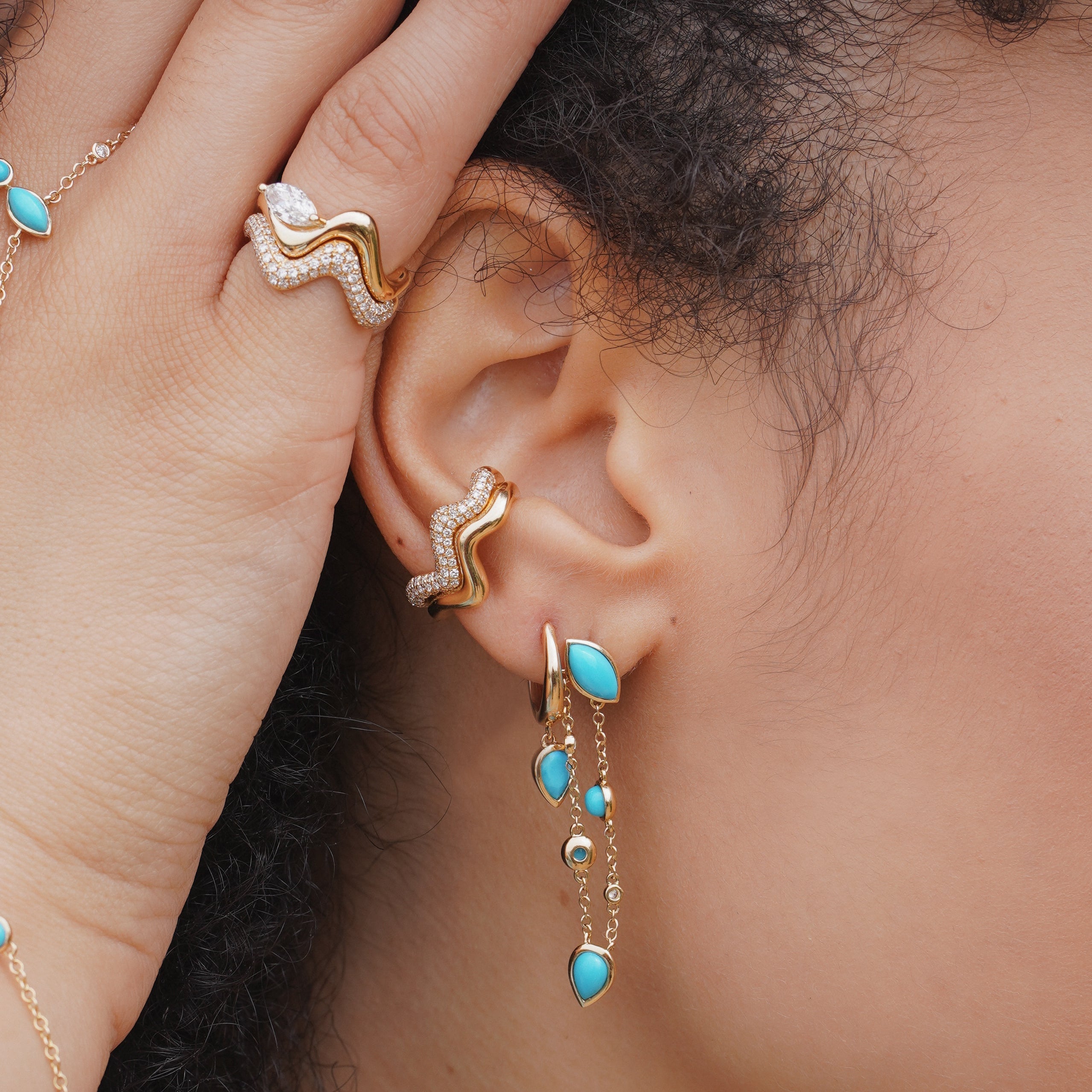 Close-up of a woman wearing gold and turquoise jewelry, including earrings and a bracelet.