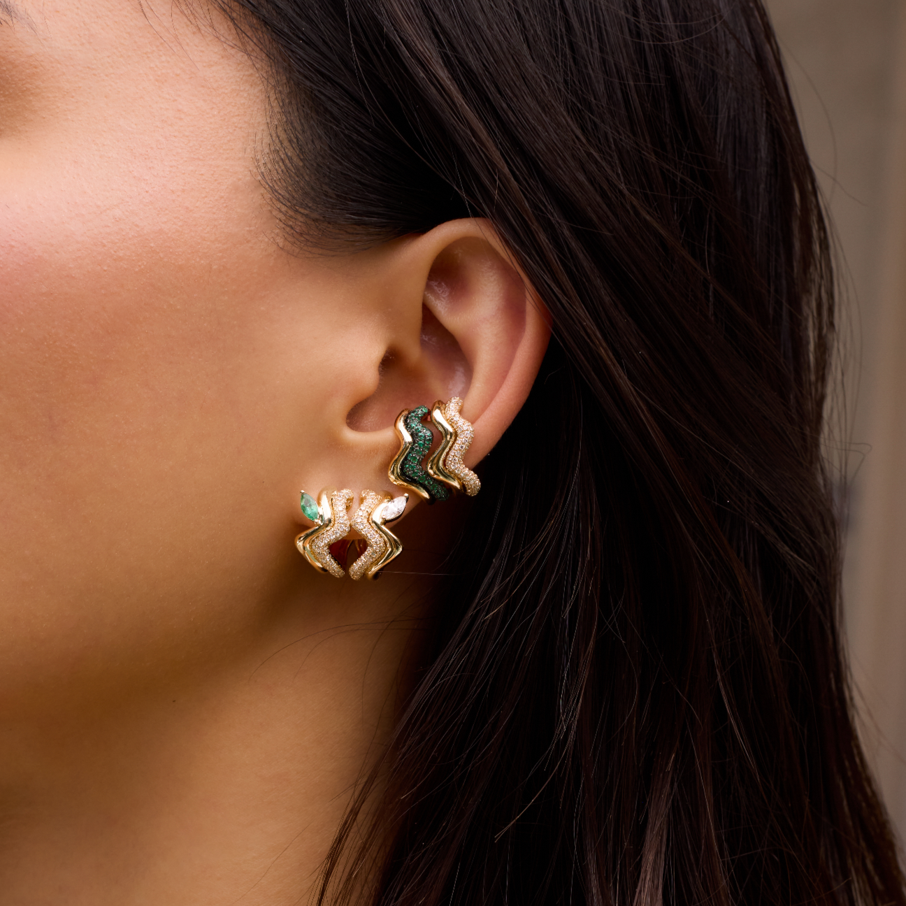 Close-up of a woman wearing gold earrings and necklaces against a neutral background