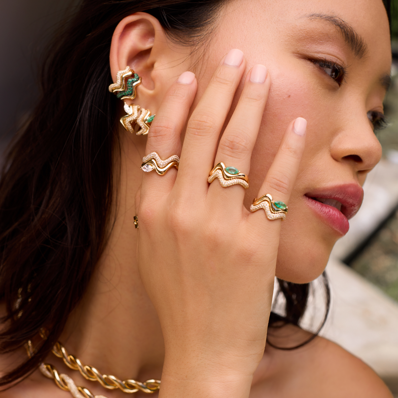 Woman wearing gold jewelry including rings and bracelets with a blurred background